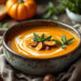 Bol rustique de soupe crémeuse au potiron et aux châtaignes, garni d'un tourbillon de crème, de morceaux de châtaigne grillée et de feuilles de sauge, posé sur une table en bois avec du pain croustillant, lumière chaude et naturelle.
