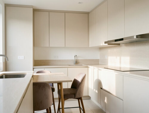 Cuisine moderne et lumineuse avec rangements intégrés, évier, plaque, hotte et coin repas harmonieux baigné de lumière naturelle.