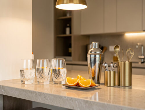 Coin bar élégant aménagé dans une cuisine moderne, avec des verres, des agrumes et des accessoires métalliques disposés sur un plan de travail en pierre.