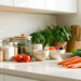 Cuisine lumineuse et bien organisée avec bocaux, boîtes hermétiques, ustensiles en bois et légumes frais disposés sur un plan de travail.