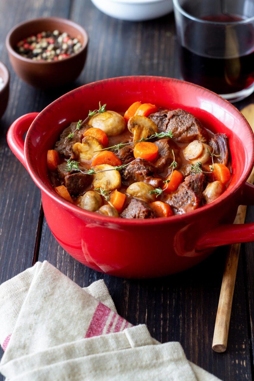 Un faitout de bœuf bourguignon mijote aux côtés d’une bouteille de vin rouge et d’un verre rempli.